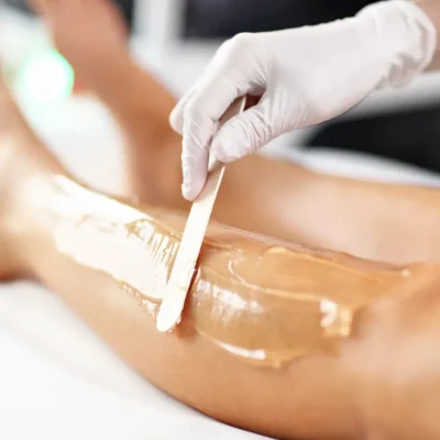 A beautician giving a wax hair removal on the leg of the woman.