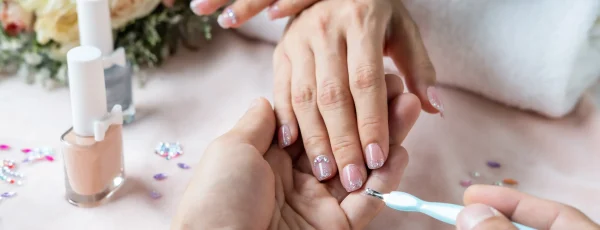 A manicurist applying a nail polish design on the hand of the client.